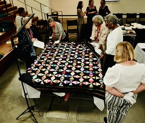 Quilter examining textile detail surrounded by African American quilts